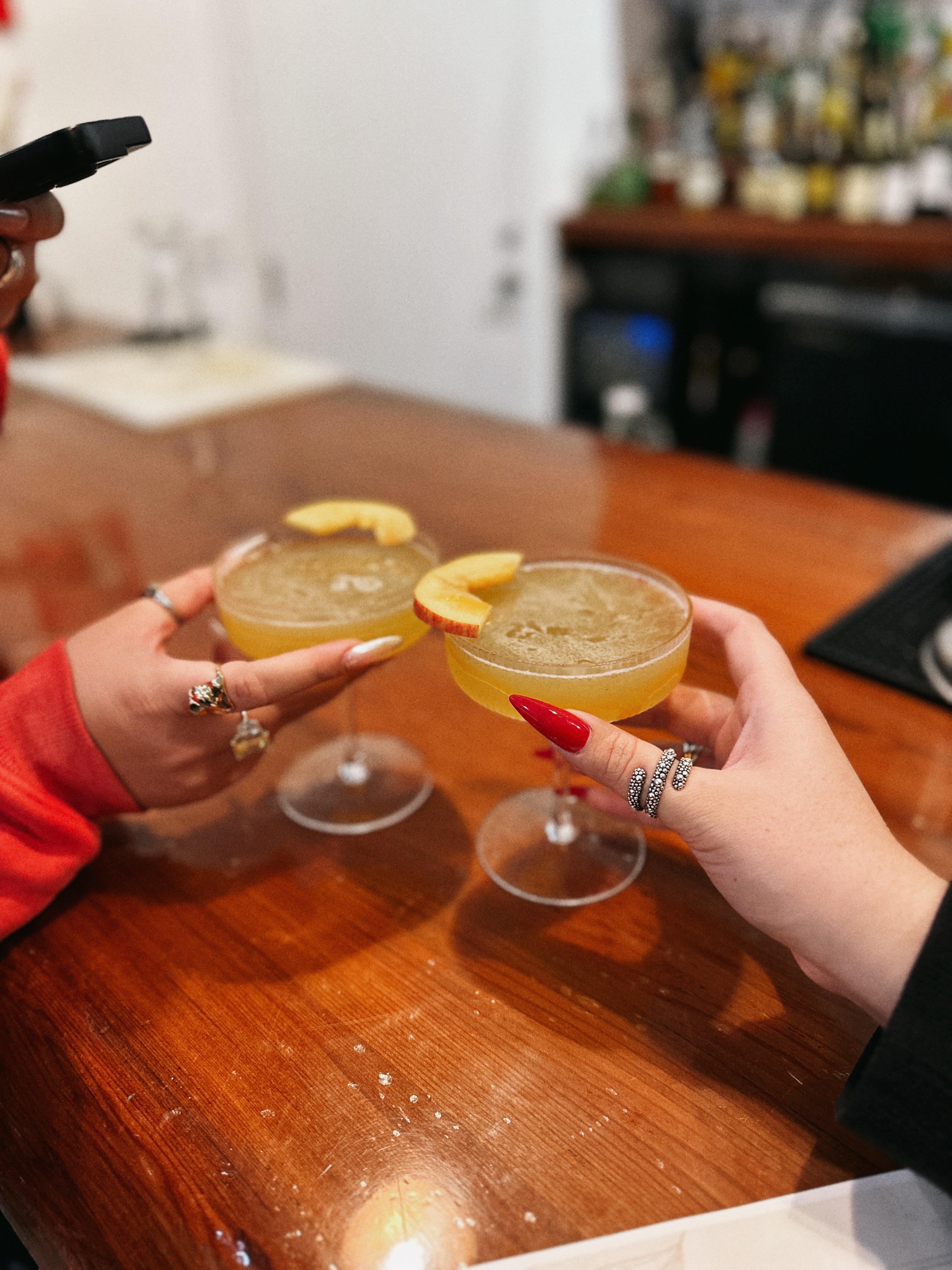 Two hands clinking glasses of yellow cocktails with orange slices on a wooden table.